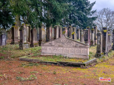 Blick durch die Gitterst&auml;be des Friedhofstors auf die dicht gereihten, teils verwitterten j&uuml;dischen Grabsteine