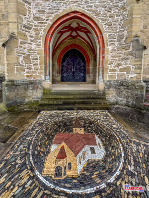 Nahaufnahme des im Bodenpflaster eingelassenen Mosaiks vor dem Kircheneingang