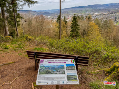 Holzsitzbank neben einer Informationstafel auf einer bewaldeten Anh&ouml;he