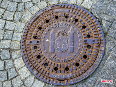 Nahaufnahme eines gusseisernen Kanaldeckels mit dem offiziellen Stadtwappen von Ilmenau