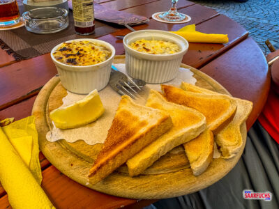 Serviertes W&uuml;rzfleisch in einer Keramikschale mit Zitronenscheibe und Toastbrot auf einem Holzbrett