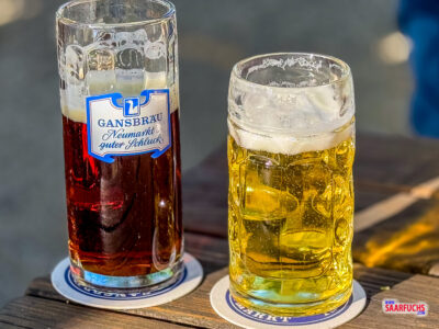 Ein gedeckter Holztisch im schattigen Biergarten des "Unteren Ganskellers" mit Blick auf Bierkrüge