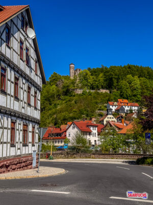 Blick von der Ortsmitte hinauf zur mittelalterlichen Burgruine Hallenburg auf bewaldetem Felsen