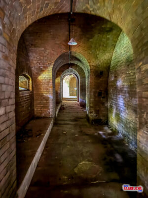 Blick durch einen langen, sp&auml;rlich beleuchteten Gang aus Ziegelmauerwerk im Fort Hahneberg