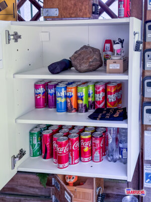 Blick in einen ge&ouml;ffneten Holzschrank mit kostenloser Verpflegung und einer Ausr&uuml;stungsbox f&uuml;r Geocacher