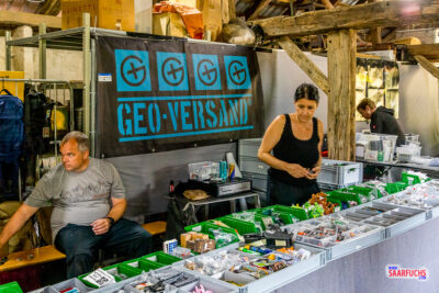 Ein gut sortierter Verkaufsstand vom GEO-VERSAND mit Geocaching-Zubehör und Behältern