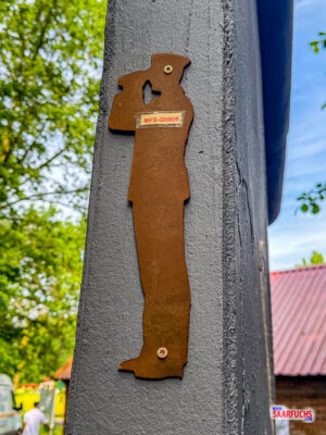Eine kleine, angeschraubte Holzfigur eines MfS-Mitarbeiters mit einer gut sichtbaren Nummer als Labcache-Station