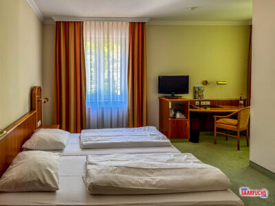 Blick in das geräumige Hotelzimmer im ersten Stock mit Holzkreuzschreibtisch, Stuhl und Blick aus dem Fenster