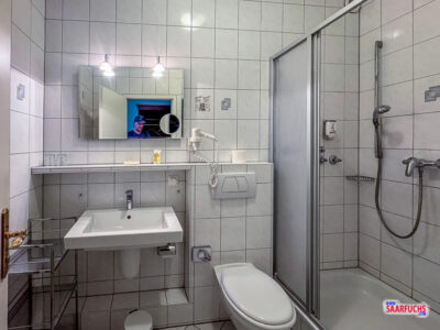 Das modern geflieste Badezimmer des Hotelzimmers mit einer gläsernen Duschkabine und Waschbecken