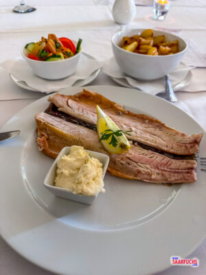 Ein Teller mit warm geräucherten Forellenfilets, Meerrettich, goldbraunen Bratkartoffeln und einer Salatbeilage