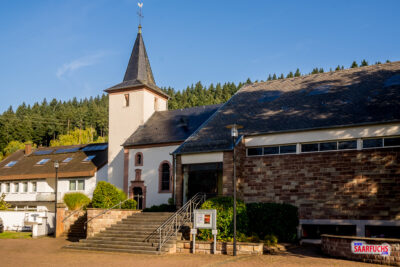 Wanderparkplatz in der Ortsmitte von Rimlingen mit Blick auf die Pfarrkirche Hl. Kreuz