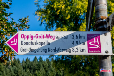 Wegweiser des Oppig-Gr&auml;t-Wegs mit Kilometerangabe 13,6 km und Richtungsweisern