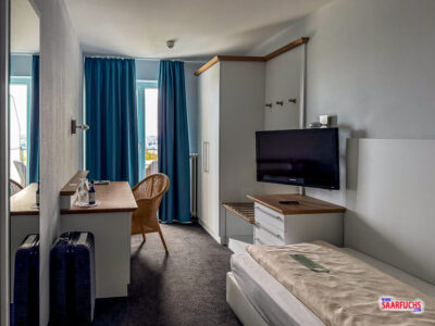 Modern eingerichtetes Einzelzimmer im Hotel mit Schreibtisch und Ablagefläche für den Koffer