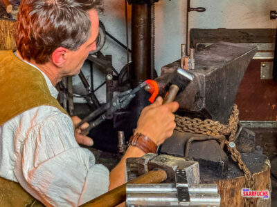 rot glühendes Eisen wird mit Hammer und Zange bearbeitet in der Schau-Schmiede der Grube Bindweide