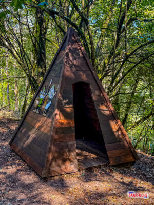 Aus Holzstämmen gebautes Wigwam im Wald mit sichtbaren Bodenplanken