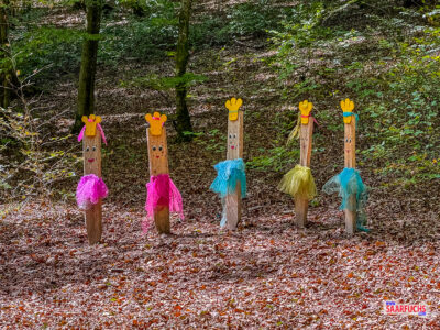 Fünf bunt gestaltete Holzkobolde nebeneinander aufgereiht am Pfad
