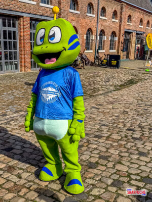 Geocaching Maskottchen Signal the Frog mit seinem Helfer auf dem Außengelände des Events