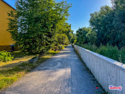 Ein asphaltierter Weg führt verkehrsberuhigt hinter Wohnhäusern entlang