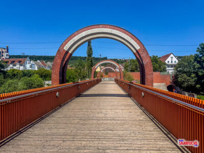 Eine moderne Fußgängerbrücke führt über den Neckar in den Landschaftspark Bruckenwasen