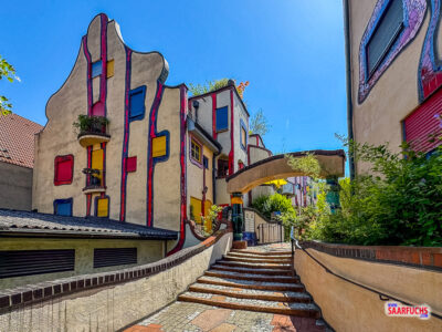 Nahaufnahme des Hundertwasser-Baus mit verzierten Säulen und bepflanzten Fenstern